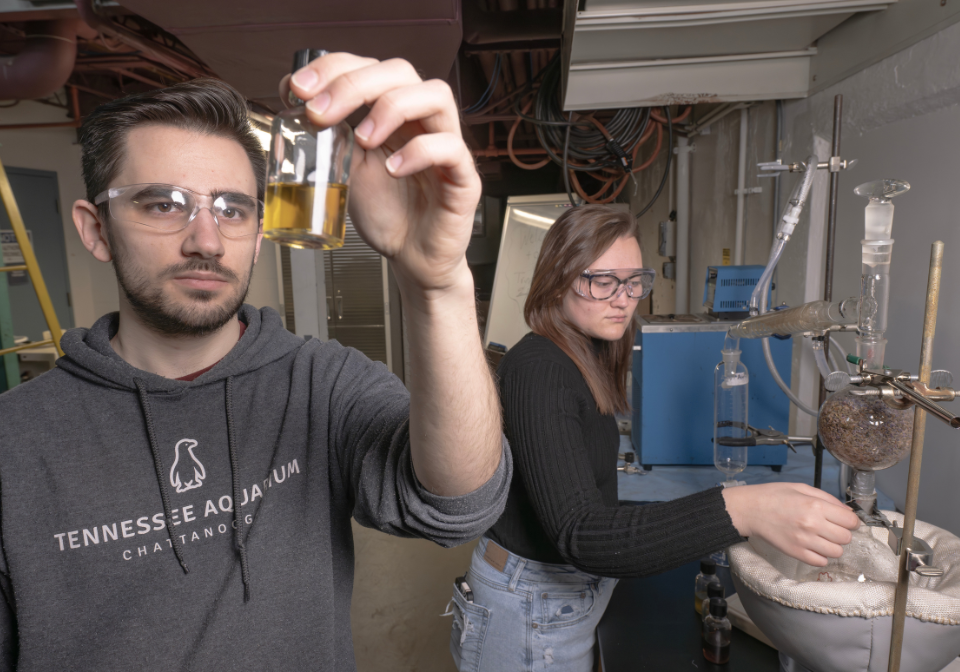 student check beaker of lavender oil while other student checks larger machine