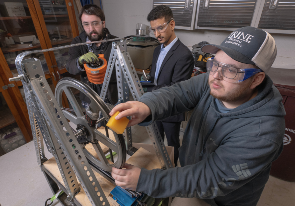 three students coat a machine in a chemical coating