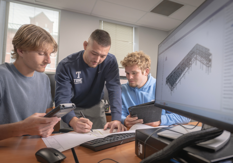 three students study a building plan for trine's new pellegrino student design center