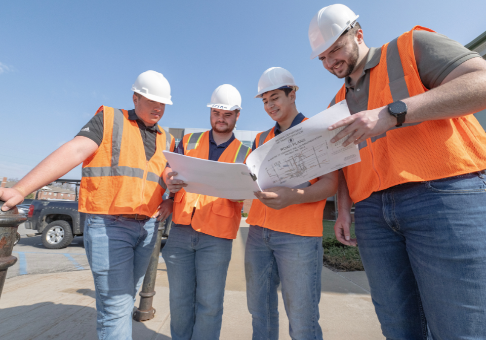 four students in safety vest study a map of trine's parking lots