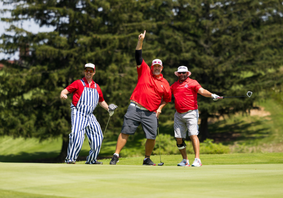 three men pose for the camera on the golf course
