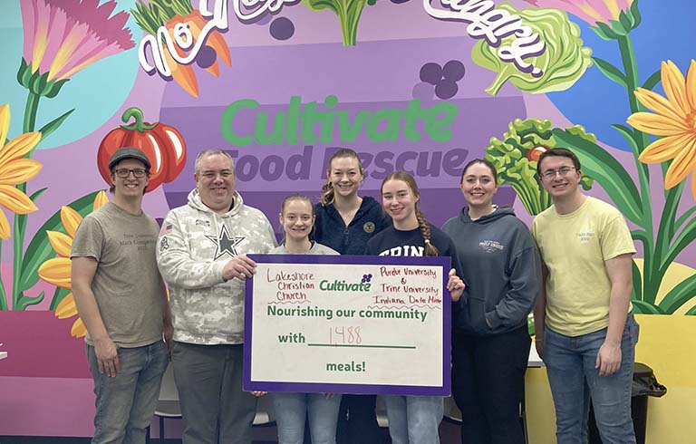 Trine students with card showing number of meals packed