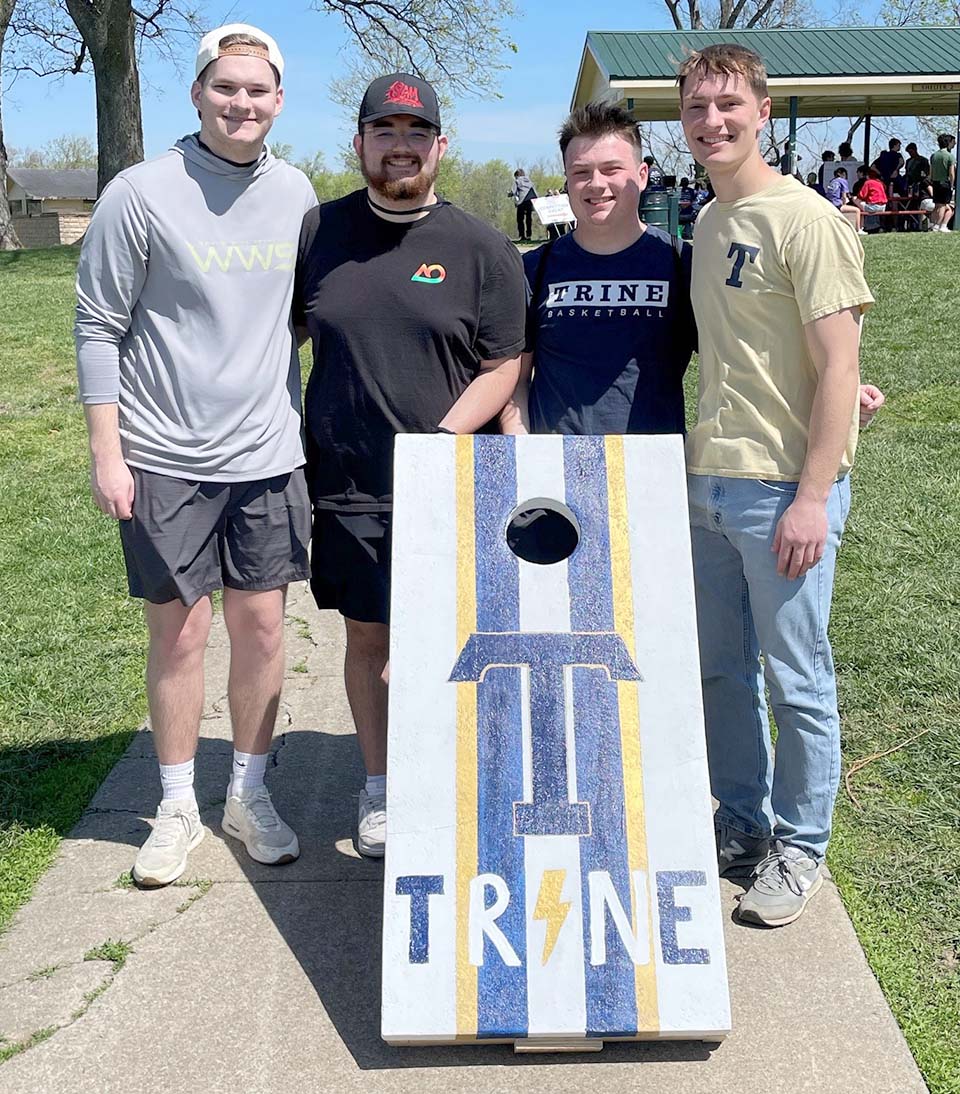 Four students standing behind concrete cornhole