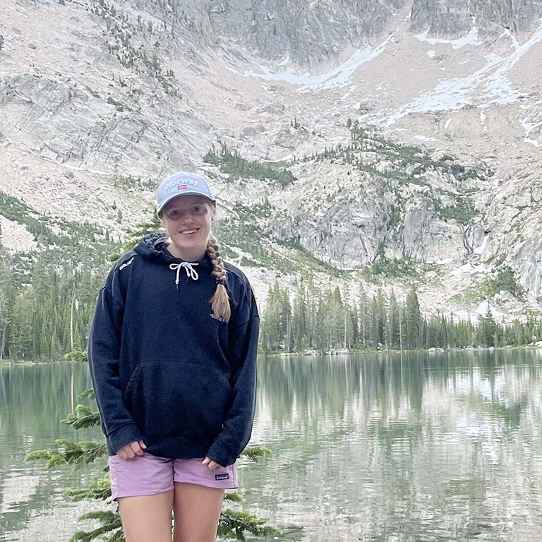 Female student standing in front of beautiful mountains and lake