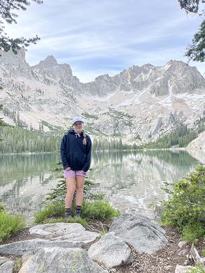 Female student standing in front of beautiful mountains and lake