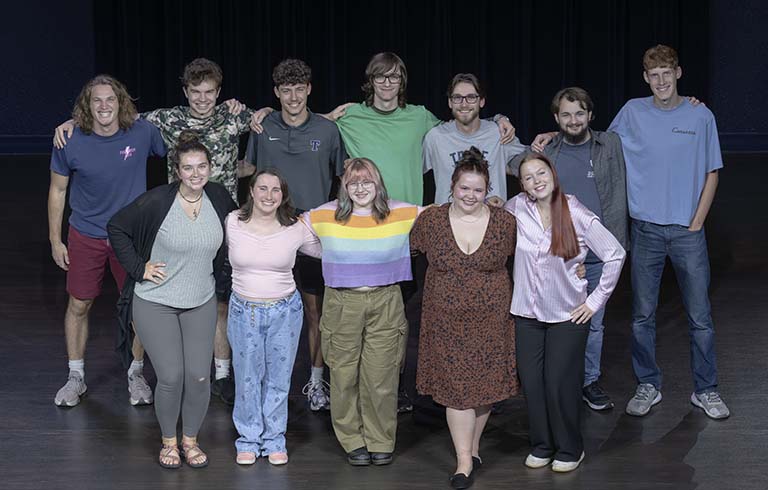 Two rows of cast members on theatre stage