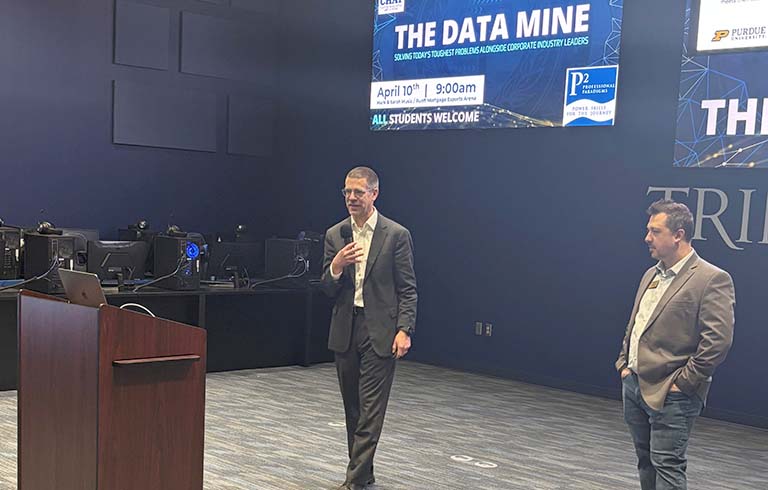 Two men speaking in front of large screen that says "The Data Mine"