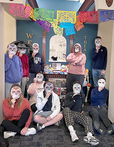 Students with traditional masks standing in front of ofrenda