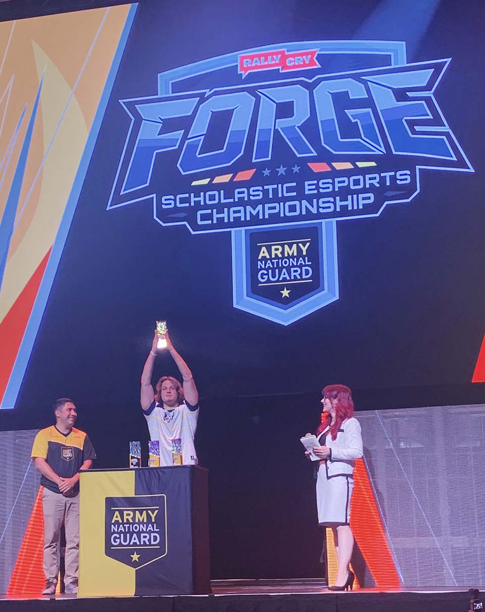 Student holding trophy up in the middle of two esports officials.