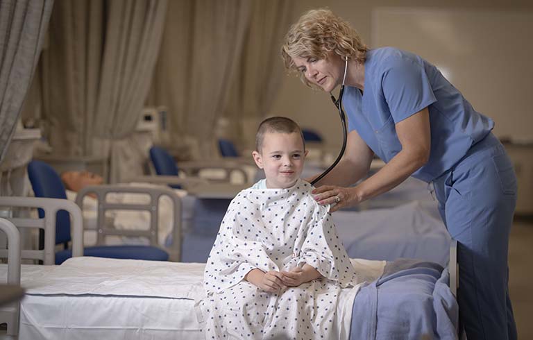 Nurse practitioner with stethoscope placed on back of young boy