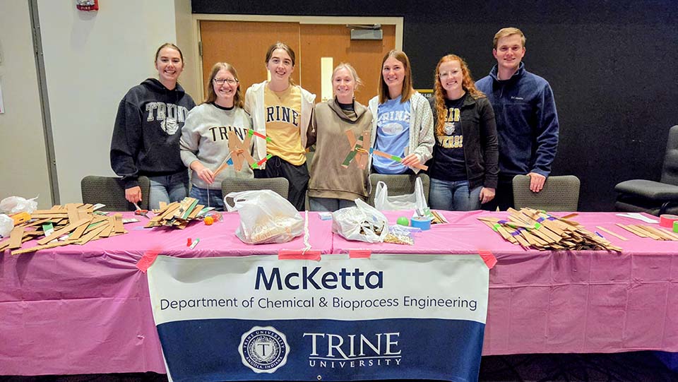 Students standing behind table with pink tablecloth and McKetta Department banner