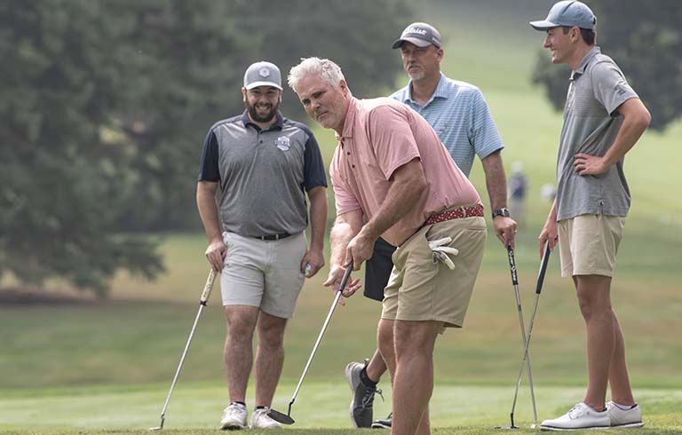 Man putting on a golf course as three others watch