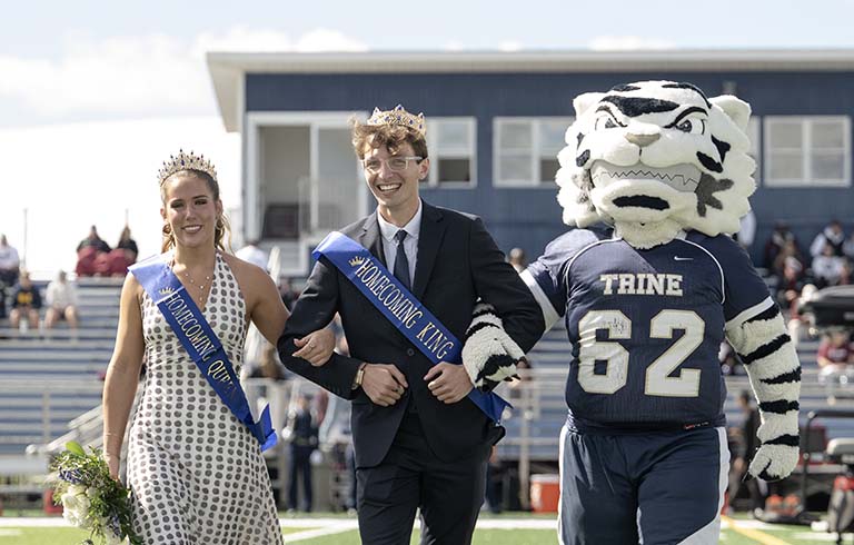 Woman and man in crowns and sashes walking arm-in-arm with white tiger mascot.