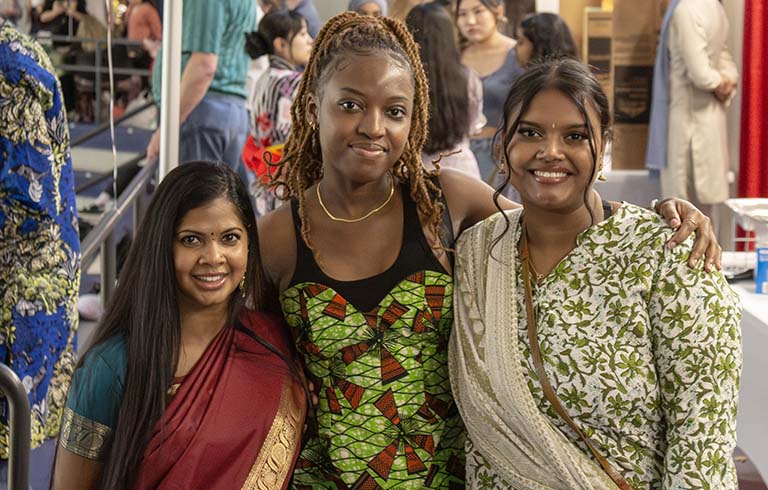 Three international students in front of tables and decorations