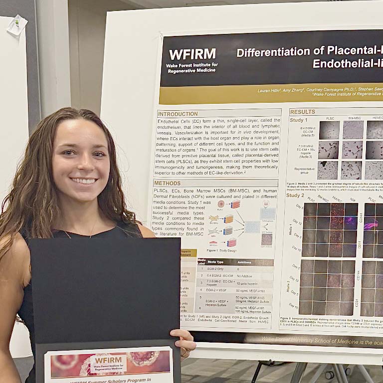 Female student holding certificate, standing in front of research poster
