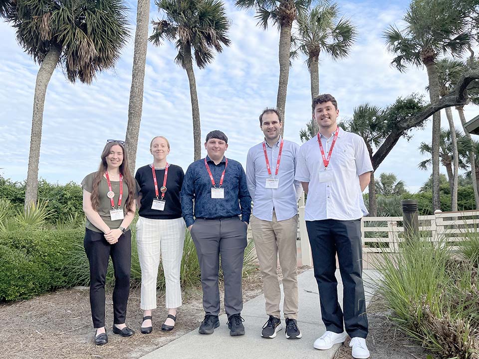 Four students and one faculty member standing in front of palm trees