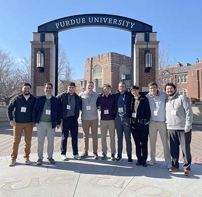 Professor and eight students in front of arch on Purdue University campus