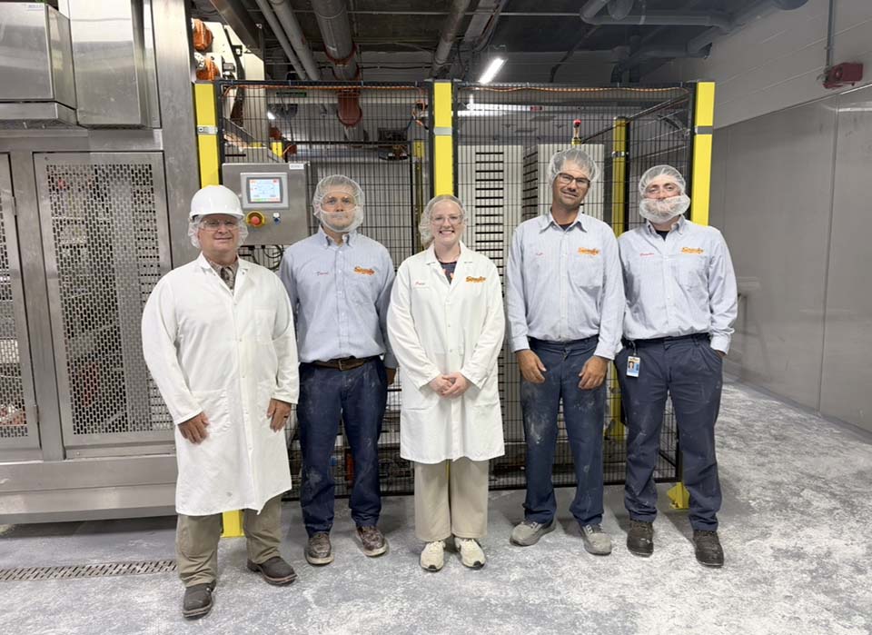 Student standing with Spangler Candy employees near production line